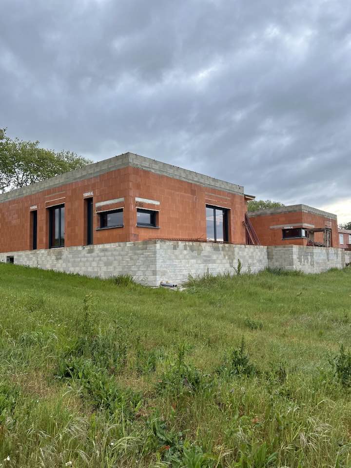 Gros œuvre maison : briques rouges Terreal sur fondation. Construction de deux maisons modernes en briques rouges Terreal. Gros œuvre sur soubassement gris sur terrain en pente. Ciel gris.