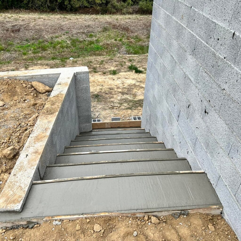 Escalier extérieur en béton coulé : fondations et murs Construction d'un escalier extérieur en béton fraîchement coulé. Murs de soutènement en parpaings. Accès au sous-sol.
