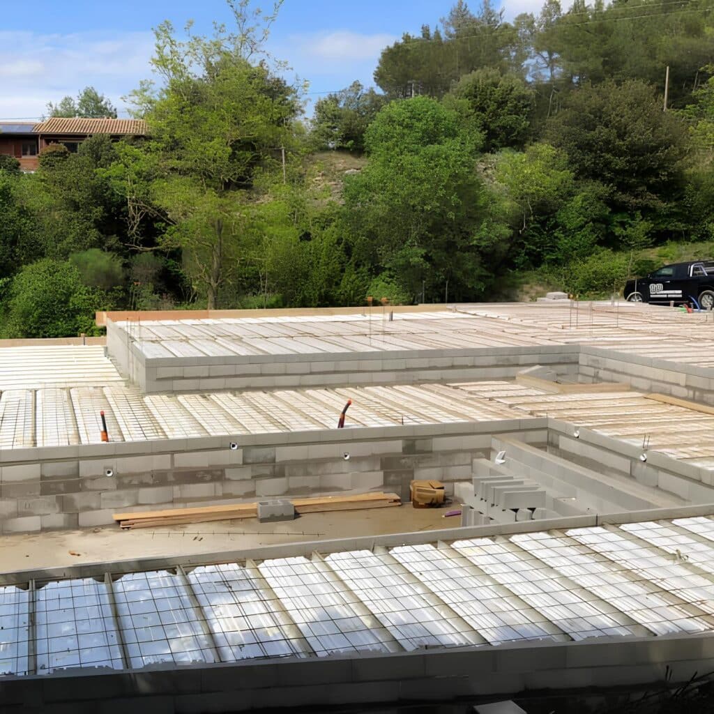 Gros œuvre : construction dalle et piscine en coffrage. Gros œuvre d'une maison et piscine. Dalle et bassin en coffrage isolant avec ferraillage prêt à couler, devant un flanc de colline boisé.