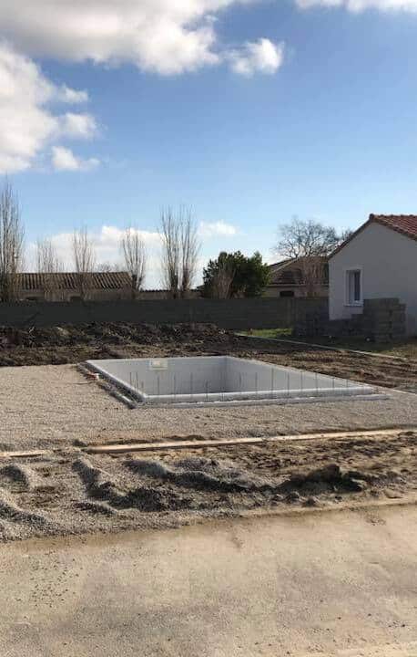 Piscine béton : Fondation et gros œuvre sur chantier. Fondations en béton d'une piscine en construction sur un chantier. Le terrain est recouvert de gravier, près d'une maison récente.