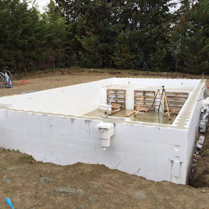 Piscine en coffrage isolant (ICF) : Fondation et murs posés. Chantier de construction d'une piscine en coffrage isolant (ICF). Murs blancs montés, fond en béton coulé et skimmer visible.